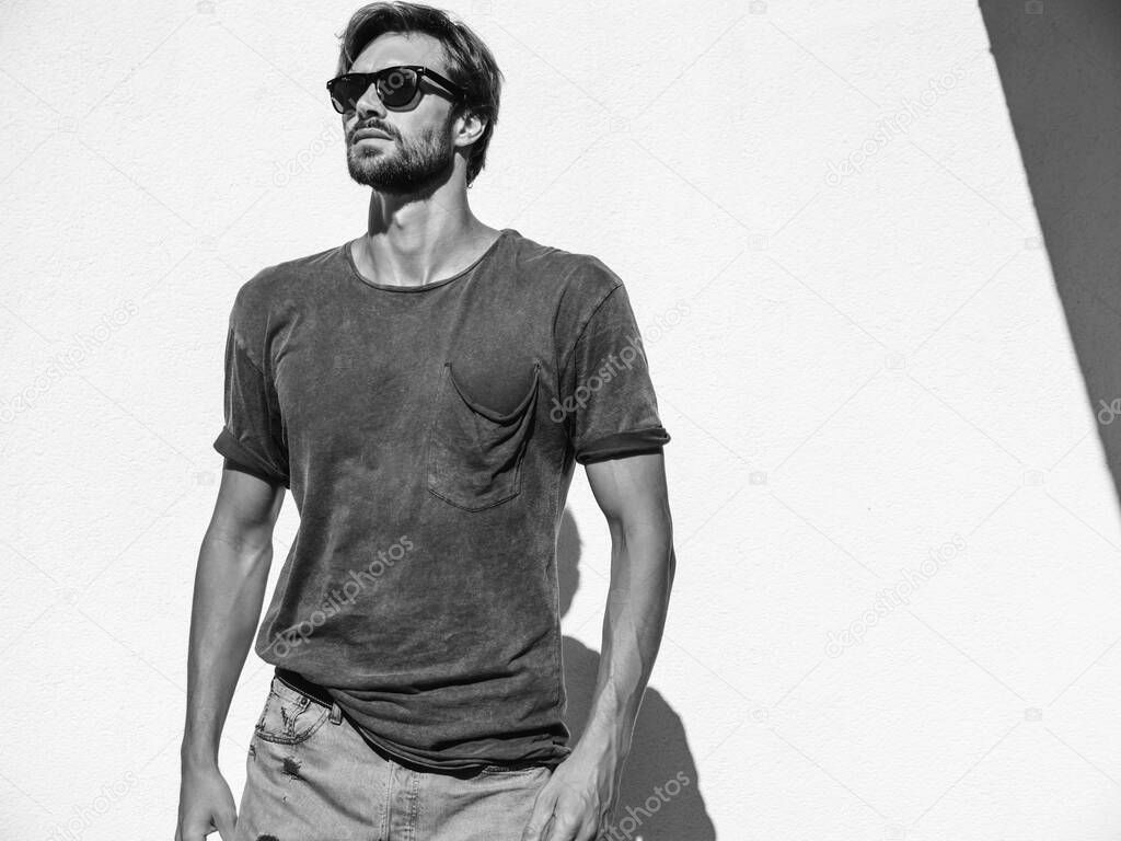 Portrait of handsome confident stylish hipster lambersexual model.Man dressed in T-shirt. Fashion male posing in the street near white wall outdoors in sunglasses