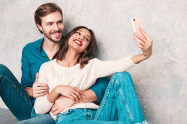 Gülümseyen güzel kadın ve yakışıklı erkek arkadaşı. Mutlu mutlu aile stüdyoda gri duvarın yanında oturuyor. Sevgililer Günü. Mankenler sarılıyor. Aşk kavramı. Selfie çekiyorlar.