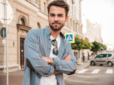 Yakışıklı, gülümseyen stil sahibi Lambersex modelinin portresi. Beyaz tişört giyen adam. Moda erkeği sokakta poz veriyor. Çapraz kollar