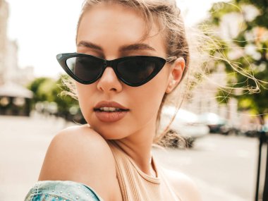 Yaz hippi kot ceketi giymiş güzel gülümseyen bir modelin yakın plan portresi. Sokakta poz veren modaya uygun bir kadın. Komik ve pozitif kadın güneş gözlükleriyle eğleniyor.