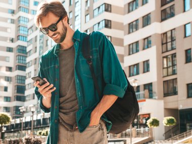 Yakışıklı, şık, havalı, lamberseksüel bir model. Tişört giymiş bir adam. Beyaz duvarın yanında sokakta poz veren bir erkek. Cep telefonunda tutuyor, kaydırıyor ve mesaj atıyor. Akıllı telefondan mesaj yazar