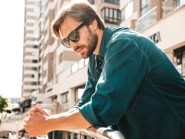 Yakışıklı, gülümseyen stil sahibi Lambersex modelinin portresi. Yeşil tişörtlü adam. Moda erkek gökdelenin arkasında güneş gözlükleriyle poz veriyor.