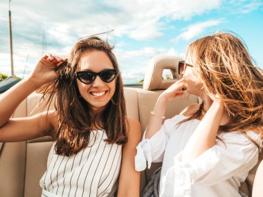 Üstü açık arabadaki iki güzel ve gülümseyen hippi kadının portresi. Cabriolet kullanan kaygısız seksi kadınlar. Pozitif modeller güneş gözlükleriyle geziyor ve eğleniyorlar.