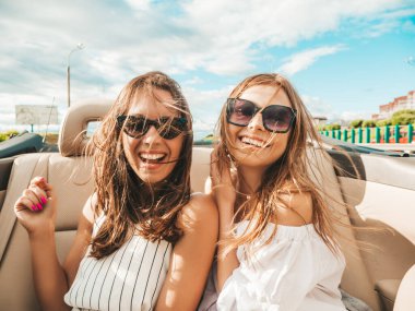 Üstü açık arabadaki iki güzel ve gülümseyen hippi kadının portresi. Cabriolet kullanan kaygısız seksi kadınlar. Pozitif modeller güneş gözlükleriyle geziyor ve eğleniyorlar.