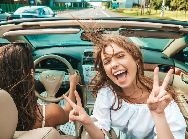 Üstü açık arabadaki iki güzel ve gülümseyen hippi kadının portresi. Cabriolet kullanan kaygısız seksi kadınlar. Pozitif modeller güneş gözlükleriyle geziyor ve eğleniyorlar.