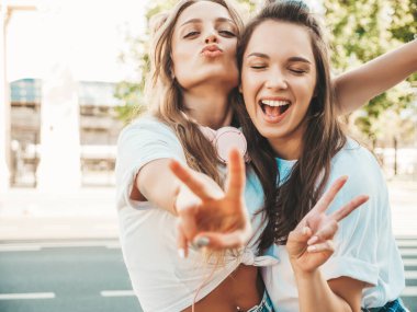 Son moda beyaz tişörtlü iki güzel gülümseyen hippi kadın portresi. Sokakta poz veren kaygısız kadınlar. Pozitif modeller eğleniyor, sarılıyor ve deliriyor.
