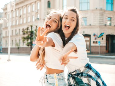 Son moda beyaz tişörtlü iki güzel gülümseyen hippi kadın portresi. Sokakta poz veren kaygısız kadınlar. Pozitif modeller eğleniyor, sarılıyor ve deliriyor.