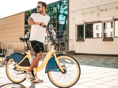 Yakışıklı, gülümseyen stil sahibi Lambersex modelinin portresi. Beyaz tişört giyen adam. Moda erkeği, arka planda güneş gözlüklü bisiklet sürüyor.