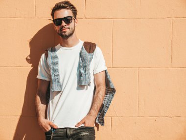 Yakışıklı, gülümseyen stil sahibi Lambersex modelinin portresi. Beyaz tişört giyen adam. Moda erkek, dışarıda güneş gözlüklü, duvarın yanında poz veriyor.