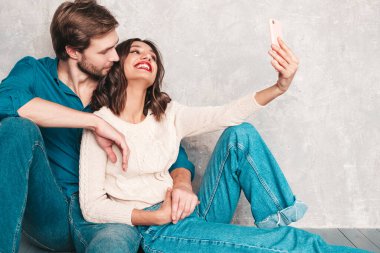 Gülümseyen güzel kadın ve yakışıklı erkek arkadaşı. Mutlu mutlu aile stüdyoda gri duvarın yanında oturuyor. Sevgililer Günü. Mankenler sarılıyor. Aşk kavramı. Selfie çekiyorlar.