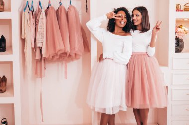 Son moda yaz elbiseleri içinde gülümseyen iki güzel uluslararası hippi kadın. Pembe gardıropta poz veren kaygısız seksi kadınlar. Pozitif modeller eğleniyor. Arkadaşlık kavramı 