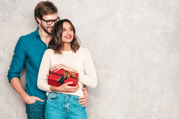 笑着漂亮的女人和她英俊的男朋友 快乐快乐的一家人在灰墙上的工作室里摆姿势 情人节 模特们拥抱并送给他女朋友的礼品盒 圣诞节 圣诞节 — 图库照片