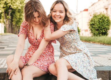 İki genç, güzel, gülümseyen yeniyetme kadın, son moda yaz kıyafetleri içinde. Sokakta arka planda merdivenlerde oturan kaygısız kadınlar. Pozitif modeller eğleniyor ve sarılıyorlar.