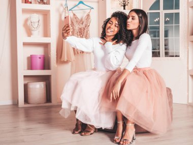 Son moda yaz elbiseleri içinde gülümseyen iki güzel uluslararası hippi kadın. Pembe gardıropta poz veren kaygısız seksi kadınlar. Pozitif modeller eğleniyor. Arkadaşlık kavramı. Selfie çekiyorlar.