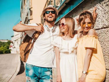 Sokakta poz veren üç genç arkadaş grubu. Moda adamı ve sıradan yaz kıyafetleri giymiş iki tatlı kadın. Gülümseyen modeller güneş gözlükleriyle eğleniyorlar. Neşeli kadınlar ve açık hava adamı.