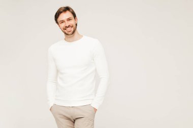 Beyaz süveter ve pantolon giyen yakışıklı, gülümseyen hippi, keresteci iş adamı modeli portresi. Stüdyoda gri arka planda poz veren modacı.