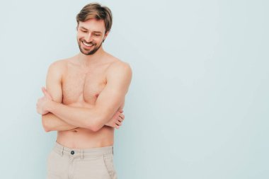 Yakışıklı, güçlü bir adamın portresi. Sağlıklı gülümseyen atletik spor modelinin açık mavi duvarın yanında poz vermesi. Çıplak gövdesi olan kendine güvenen seksi moda erkeği. Lambersexual stüdyoda.