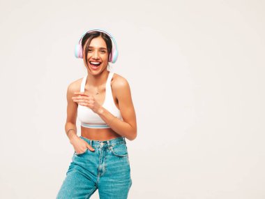 Kot pantolon giymiş, gülümseyen güzel bir kadın. Kablosuz kulaklıkla müzik dinleyen seksi tasasız model. Stüdyoda gri arka planda poz veren sevimli ve pozitif kadın.