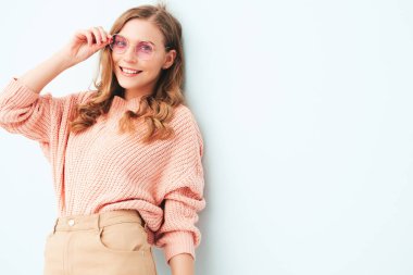 Modayı takip eden yaz hippi kıyafetleri içinde gülümseyen genç bir kadının portresi. Stüdyoda açık mavi duvarın yanında poz veren kaygısız bir kadın. Güneş gözlükleriyle evde eğlenen pozitif model. Neşeli ve mutlu.