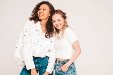 Moda kıyafetleri içinde iki güzel, gülümseyen uluslararası hippi kadın. Stüdyoda gri arka planda poz veren kaygısız seksi kadınlar. Pozitif modeller eğleniyor. Arkadaşlık kavramı 