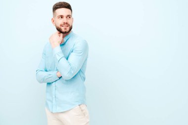 Yakışıklı, gülümseyen hippi, keresteci iş adamı modelinin portresi. Günlük gömlek ve pantolon giyiyor. Moda tarzı bir adam stüdyoda açık mavi duvara karşı poz veriyor.