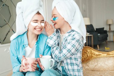 Gözlerinin altında bantlarla gülümseyen iki genç kadın. Lüks bir dairede yatağında oturan kaygısız mankenler. Evde havlularla kafalarının üstünde güzellik tedavisi yapıyorlar. Çay içiyor, bardak tutuyor.