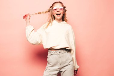 Kameraya bakan genç ve güzel bir kadının portresi. Hippi kıyafetleriyle gülümseyen modaya uygun bir kadın. Güneş gözlükleriyle pembe duvarın yanında poz veren pozitif ve komik bir model. Mutlu ve neşeli.