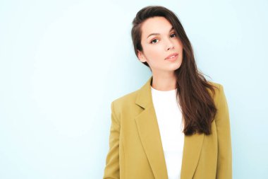 Moda kıyafetleri içinde gülümseyen genç ve güzel bir bayan. Stüdyoda açık mavi duvarın yanında poz veren kaygısız seksi kadın. Pozitif model içeride eğleniyor. Neşeli ve mutlu