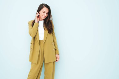 Moda kıyafetleri içinde gülümseyen genç ve güzel bir bayan. Stüdyoda açık mavi duvarın yanında poz veren kaygısız seksi kadın. Pozitif model içeride eğleniyor. Neşeli ve mutlu