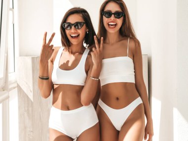 Beyaz iç çamaşırlı gülümseyen iki güzel kadının portresi. Sabahın erken saatlerinde balkonda poz veren kaygısız seksi modeller. Güneş gözlükleriyle sarılıp deliriyorlar.