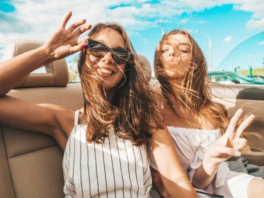 Üstü açık arabadaki iki güzel ve gülümseyen hippi kadının portresi. Cabriolet kullanan kaygısız seksi kadınlar. Pozitif modeller güneş gözlükleriyle geziyor ve eğleniyorlar.