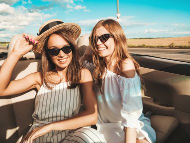 Üstü açık arabadaki iki güzel ve gülümseyen hippi kadının portresi. Cabriolet kullanan kaygısız seksi kadınlar. Pozitif modeller güneş gözlükleriyle geziyor ve eğleniyorlar.
