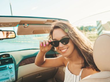 Üstü açık arabadaki güzel ve gülümseyen yeniyetme kadın portresi. Cabriolet kullanan kaygısız seksi kadın. Gün batımında güneş gözlüğüyle gezmek ve eğlenmek