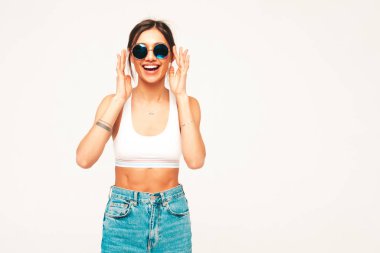 Beyaz formalı, üst tişörtlü ve kot pantolonlu güzel bir kadının portresi. Seksi kaygısız neşeli model içeride eğleniyor. Şirin ve pozitif kadın stüdyoda gri arka planda poz veriyor.