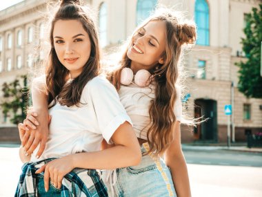 Son moda beyaz tişörtlü iki güzel gülümseyen hippi kadının portresi. Sokakta poz veren kaygısız kadınlar. Pozitif modeller eğleniyor, sarılıyor ve deliriyor.