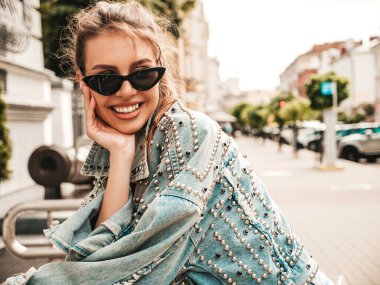 Hipster kot ceket giymiş güzel gülümseyen bir modelin portresi. Sokakta poz veren modaya uygun bir kadın. Komik ve pozitif kadın güneş gözlükleriyle eğleniyor.