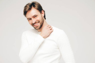 Beyaz süveter ve pantolon giyen yakışıklı, gülümseyen hippi, keresteci iş adamı modeli portresi. Stüdyoda gri arka planda poz veren modacı.