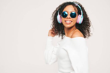 Kıvırcık saçlı güzel bir zenci kadın. Kazaklı ve kot pantolonlu bir model. Kablosuz kulaklıkla müzik dinleyen kaygısız bir kadın.