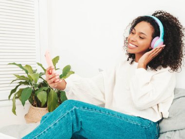 Saçları kıvırcık, saçları kıvırcık, süveter ve kot giyen, sabahları kablosuz kulaklıkla müzik dinleyen, kaygısız bir kadın.