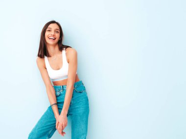 Beyaz formalı bluz ve kot pantolon giymiş güzel bir kadın. Seksi kaygısız neşeli model sabahının tadını çıkarıyor. Şirin ve pozitif kadın stüdyoda açık mavi duvarın yanında poz veriyor.