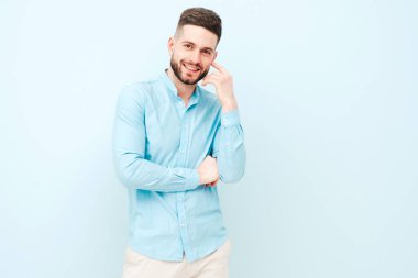 Yakışıklı, gülümseyen hippi, keresteci iş adamı modelinin portresi. Günlük gömlek ve pantolon giyiyor. Moda tarzı bir adam stüdyoda açık mavi duvara karşı poz veriyor.