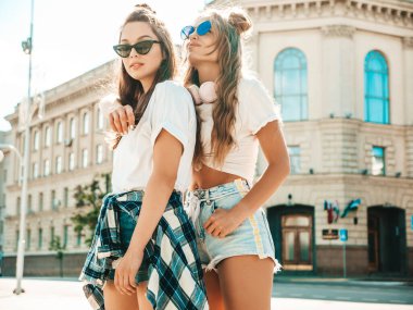 Son moda beyaz tişörtlü iki güzel gülümseyen hippi kadının portresi. Sokakta poz veren kaygısız kadınlar. Pozitif modeller eğleniyor, sarılıyor ve deliriyor.