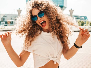 Kıvırcık saçlı, yaz hippi kıyafetleri giymiş güzel bir mankenin portresi. Sokakta poz veren tasasız bir model. Modayı takip eden eğlenceli ve olumlu kadın.