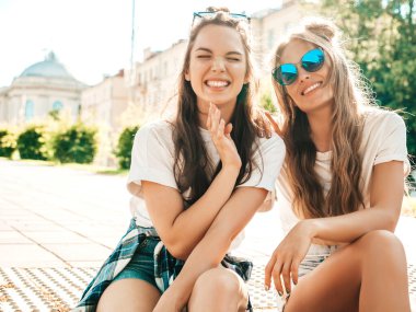 Son moda beyaz tişörtlü iki güzel gülümseyen hippi kadının portresi. Sokakta poz veren kaygısız kadınlar. Pozitif modeller eğleniyor, sarılıyor ve deliriyor.