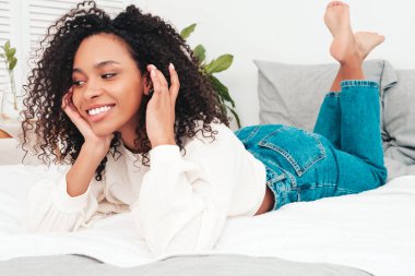 Saçları kıvırcık, güzel, siyah bir kadın. Süveter ve kotla seksi gülümseyen manken sabahları beyaz iç mekandaki lüks bir dairede ya da otel odasında yatar.