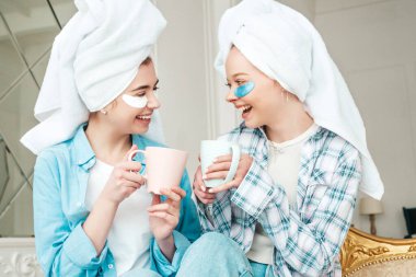 Gözlerinin altında bantlarla gülümseyen iki genç kadın. Lüks bir dairede yatağında oturan kaygısız mankenler. Evde havlularla kafalarının üstünde güzellik tedavisi yapıyorlar. Çay içiyor, bardak tutuyor.