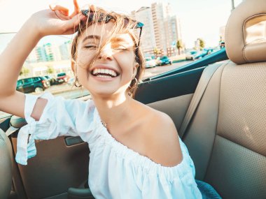 Üstü açık arabadaki güzel ve gülümseyen yeniyetme kadın portresi. Cabriolet kullanan kaygısız seksi kadın. Gün batımında güneş gözlüğüyle gezmek ve eğlenmek