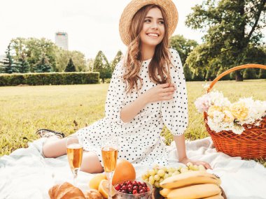 Yazlık kotlu, pembe tişörtlü ve şapkalı güzel hippi kadın. Kaygısız kadın dışarıda piknik yapıyor. Çimlerin üzerinde oturan, meyve ve peynir yiyen pozitif model.