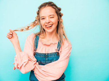 Genç ve güzel bir kadın kameraya bakıyor. Popüler bir bayan günlük kot pantolon içinde gülümsüyor. Stüdyoda mavi duvarın yanında poz veren pozitif ve komik bir model. Neşeli ve mutlu. Dil nasıl?