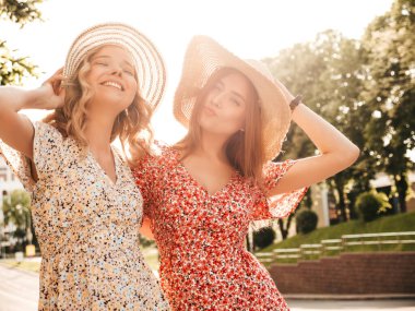 İki güzel, güler yüzlü yeniyetme kadın, şık yaz kıyafetleri içinde. Sokakta şapkalarla poz veren kaygısız kadınlar. Pozitif modeller eğleniyor ve sarılıyorlar.